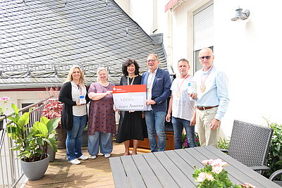 Foto einer Spendenübergabe. 6 Personen stehen auf der Terrasse des Hospizes. Eine Dame hält einen Spendenscheck über 4.000 Euro in den Händen.