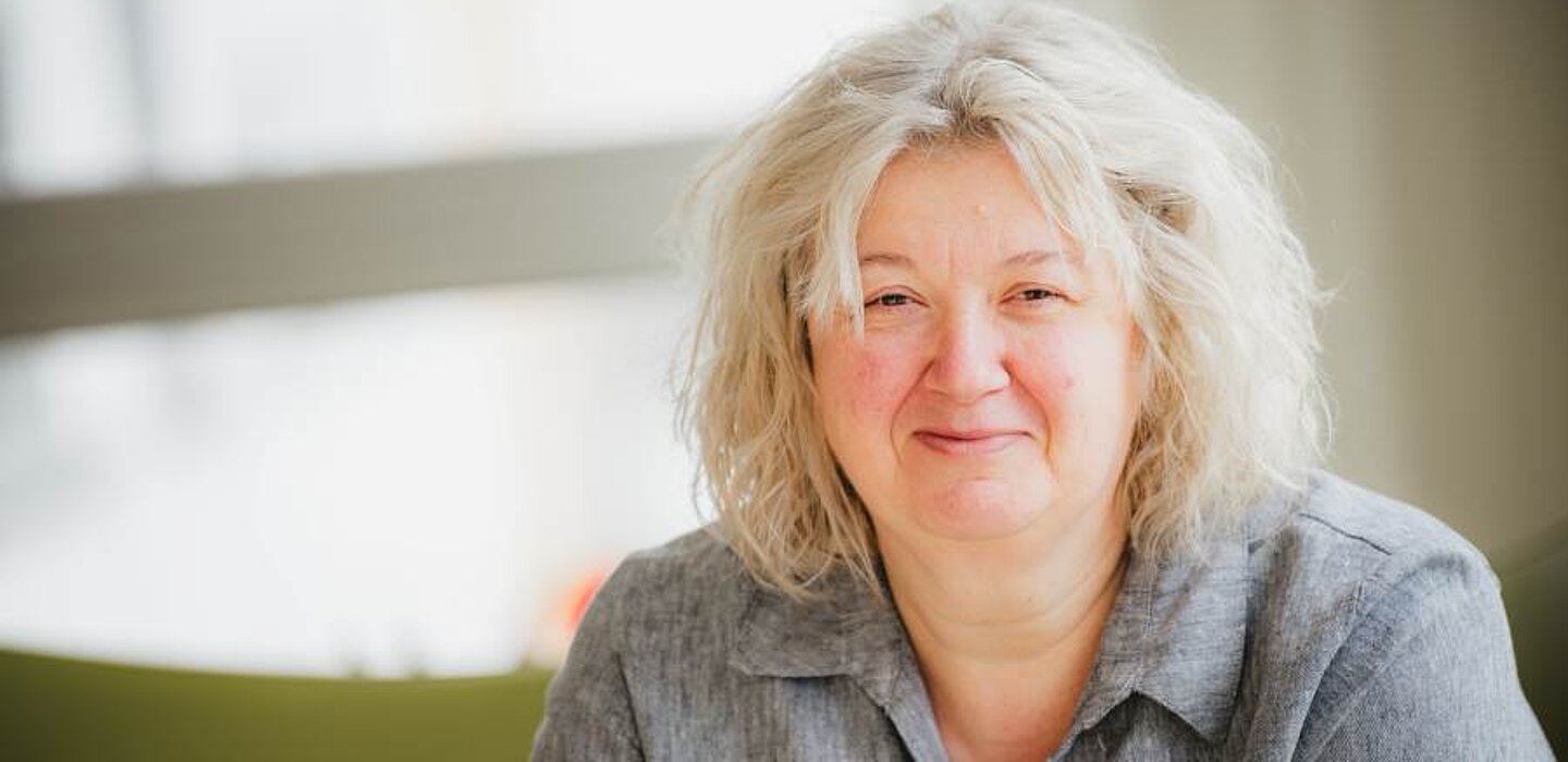 Porträtfoto von Christiane Stahl, Hospizleiterin. Sie sitzt in einem grauen Oberteil für einem teils grünem, teils weißem Hintergrund.
