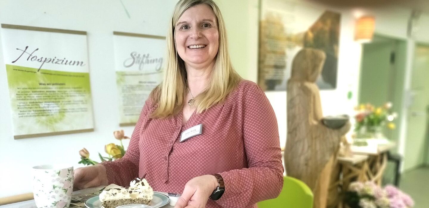 Eine ehrenamtliche Hospizbegleiterin macht sich mit Kaffee und Kuchen auf einem Tablett auf, um eine Bewohnerin zu besuchen.