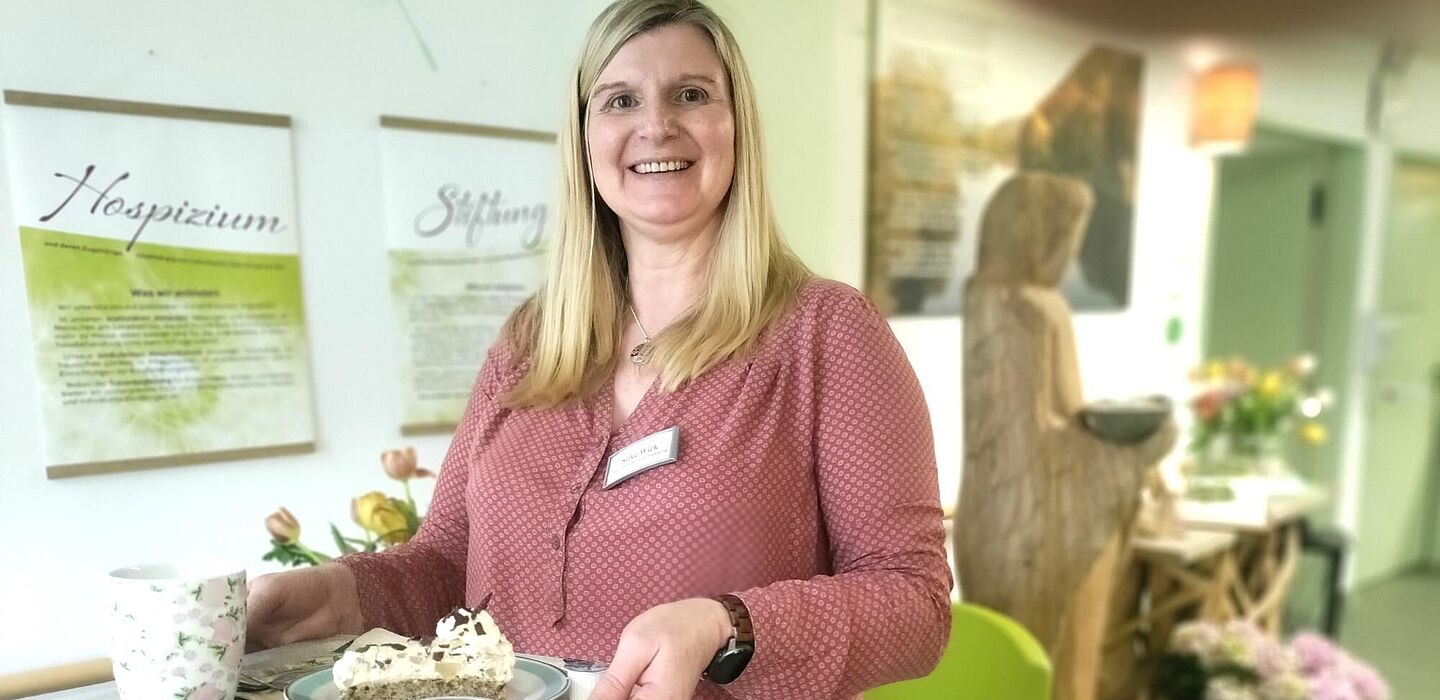 Eine ehrenamtliche Hospizbegleiterin macht sich mit Kaffee und Kuchen auf einem Tablett auf, um eine Bewohnerin zu besuchen.