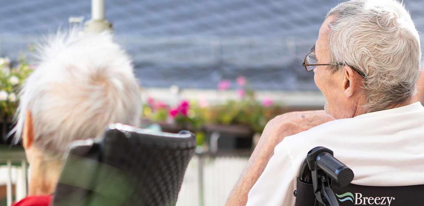 Ein Mann und eine Frau sitzen in Rollstühlen auf der Terrasse und unterhalten sich.