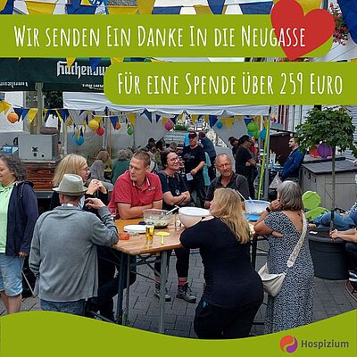 Bei einem Straßenfest stehen mehrere Menschen an einem Tisch beisammen und unterhalten sich. Es ist mit blau-gelben Wimpeln und Luftballons geschmückt und im Hintergrund sieht man einen Bierbrunnen.