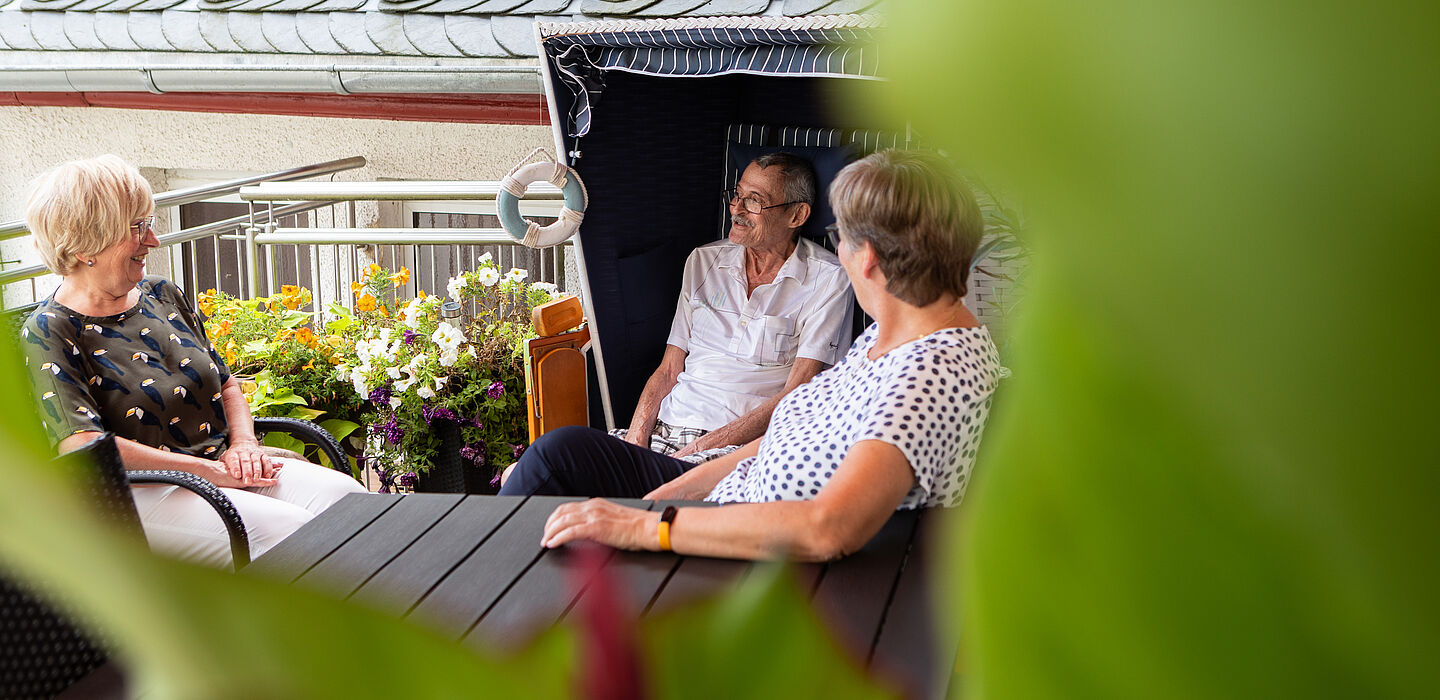 Ein Bewohner sitzt mit zwei Besucherinnen im Strandkorb auf der Terrasse.