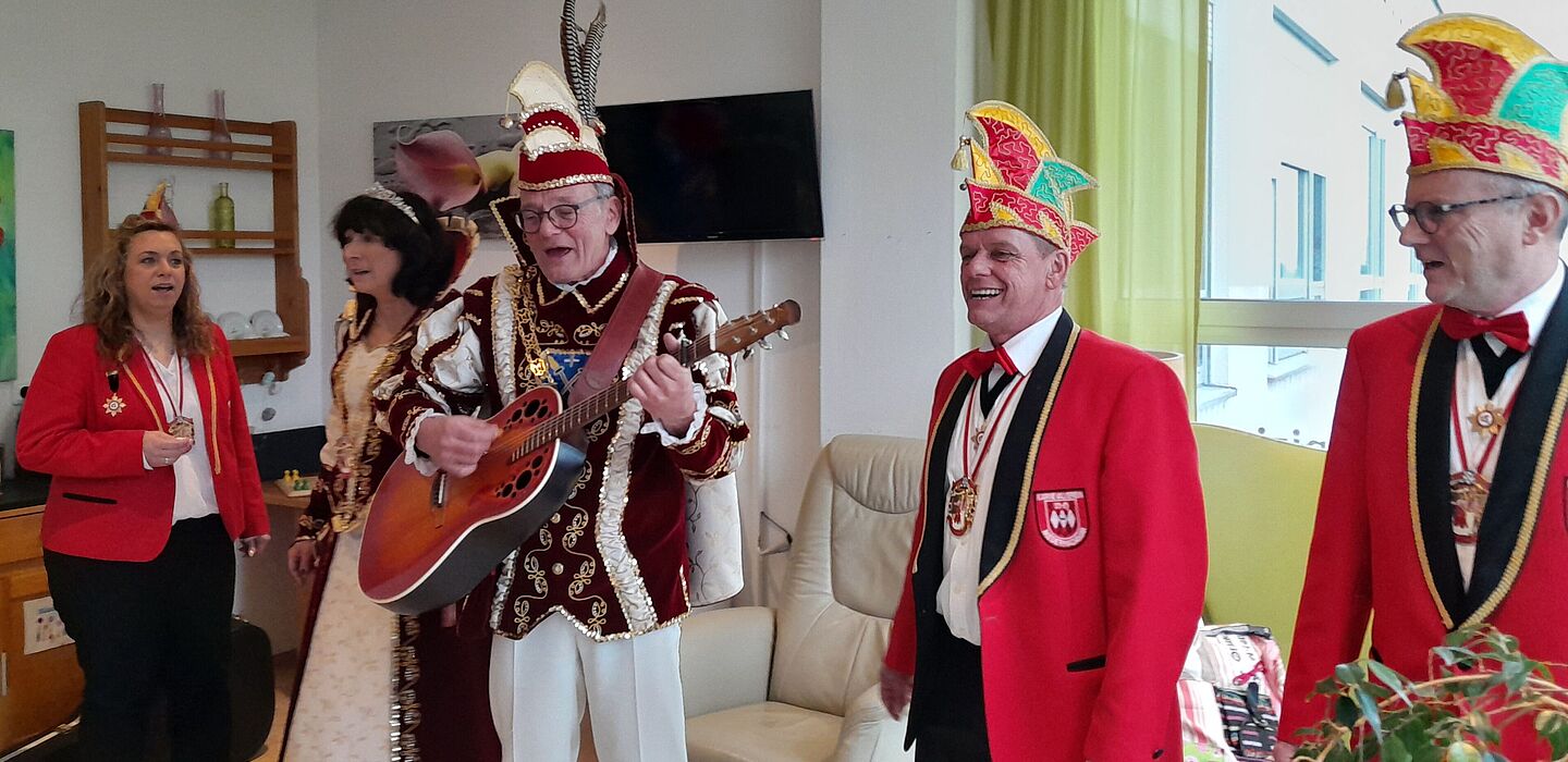 Das Karnevalsprinzenpaar und sein Hofstaat sind zu Besuch im Hospiz. Alle tragen Ihre Kostüme bzw. Uniformen. Der Prinz spielt Gitarre, alle singen.